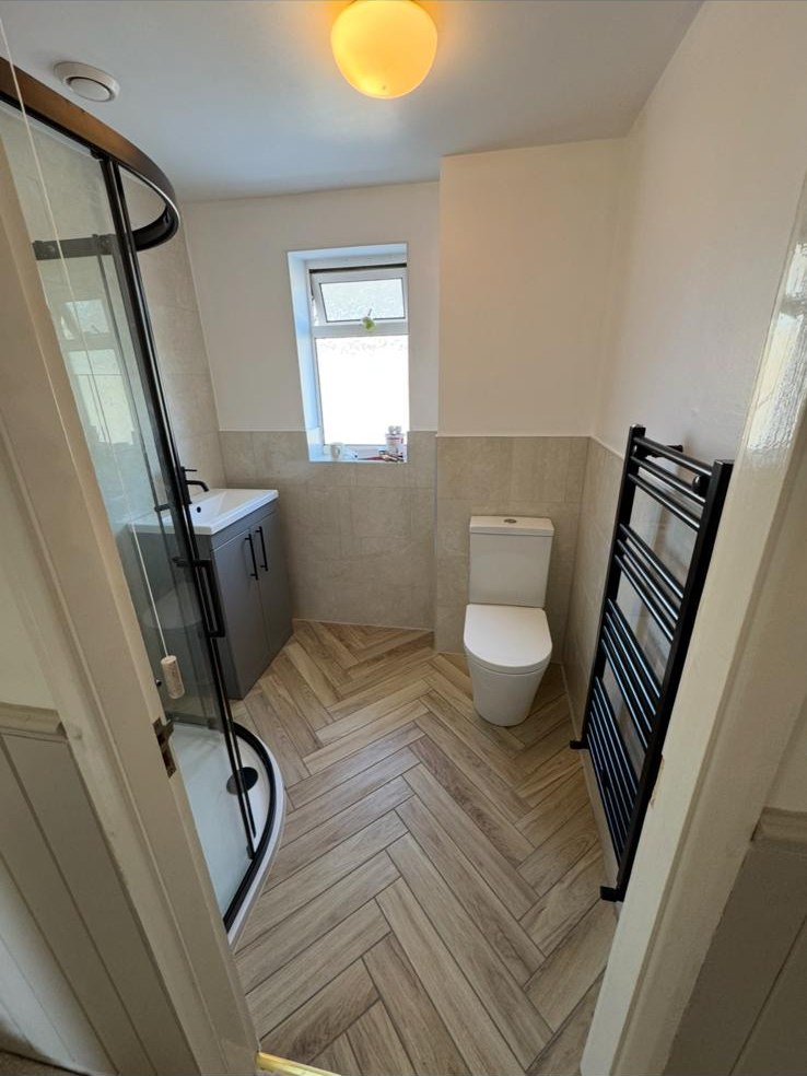 A fully fitted bathroom with walk-in shower and herringbone flooring by L.C Plumbing Services